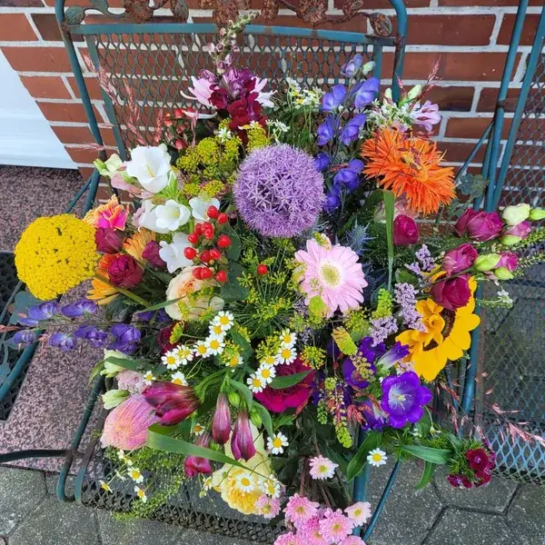 Farbenreiches Blumenarrangement mit Zierlauch, Sonnenblume und Rittersporn auf einem Gartenstuhl