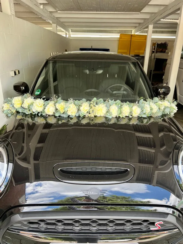 Schwarzes Hochzeitsauto mit Girlande aus weißen Blüten, Schleierkraut und Eukalyptus auf der Motorhaube