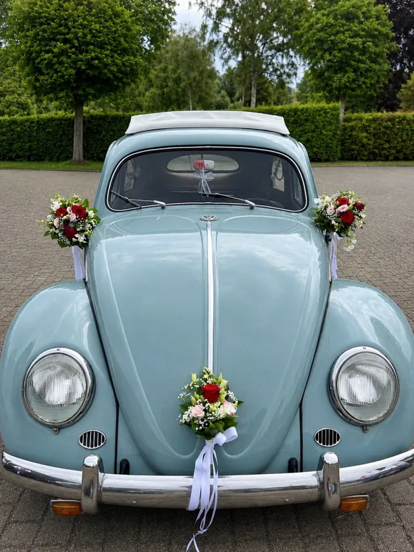 Hellblauer VW Käfer mit drei kleinen Blumengestecken aus roten Rosen, Rosé und Weiß an Haube und Spiegeln
