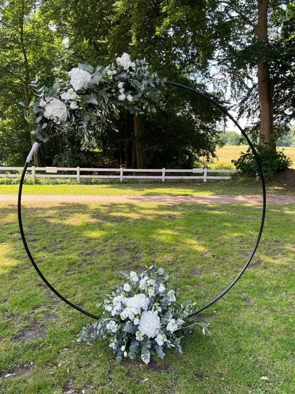 Schwarzer runder Traubogen im Garten mit asymmetrischem Schmuck aus weißen Blumen und Grün