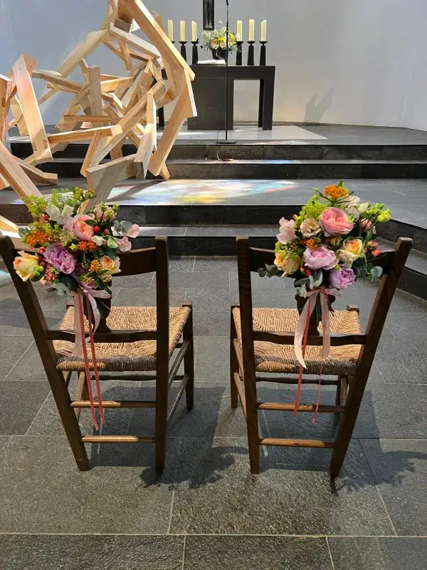 Zwei Stühle in einer Kirche mit farbenfrohen Blumengestecken und langen rosa Bändern