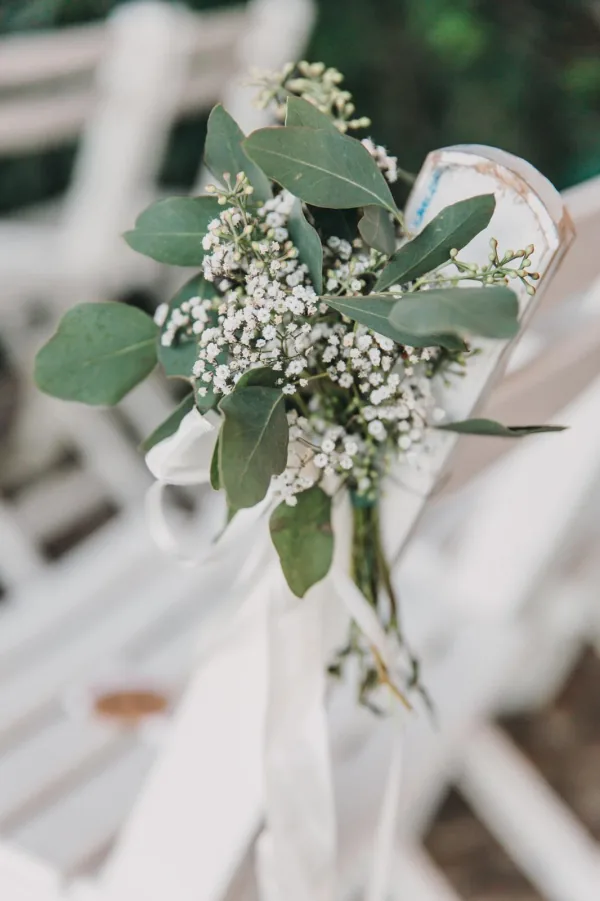 Zarter Hochzeitsschmuck aus Schleierkraut und Eukalyptus an einem weißen Stuhl