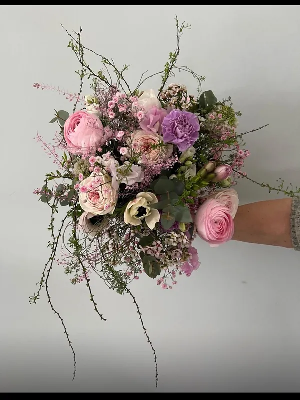 Locker gebundener Strauß in Rosa und Flieder mit Ranunkeln, Anemonen, Nelken, Eukalyptus und zarten Zweigen, gehalten von einer Floristin von Blumen Jüttemeier
