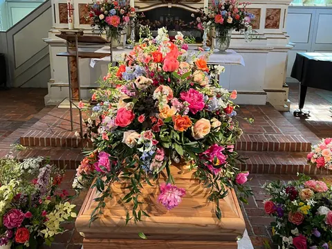 Farbenreicher Sargschmuck mit Rosen, Pfingstrosen und Rittersporn in einer Kirche