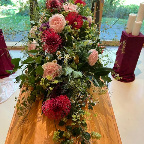 Länglicher Sargschmuck mit rosafarbenen Rosen, roten Nadelkissen und lockerem Grün